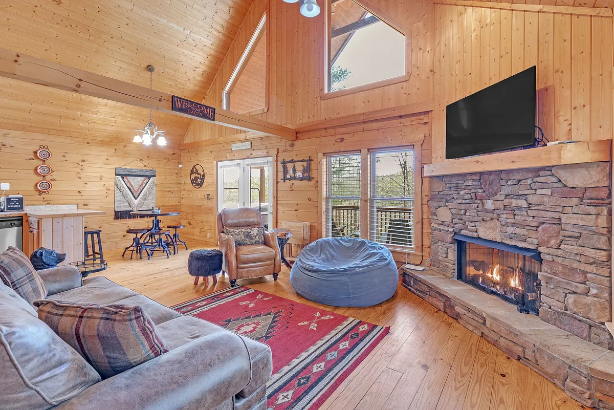 A welcoming living room with a glowing fireplace, expansive windows that let in golden sunlight, and comfortable seating arranged on a decorative rug. The setting radiates warmth and encourages relaxation, conversation, and shared moments.