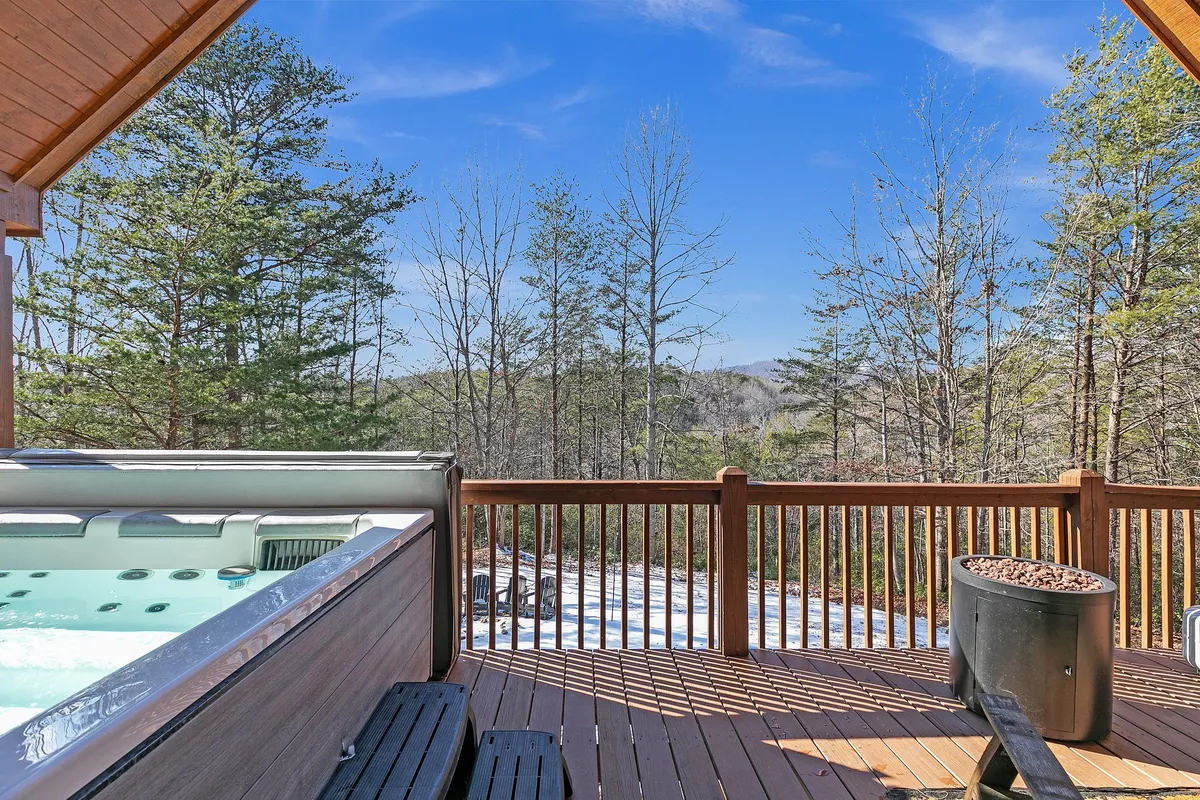 This image captures a wooden deck featuring a hot tub, with surrounding trees and a clear mountain view in the background. The serene outdoor setting suggests a tranquil environment perfect for relaxation after a day of mountain adventures.