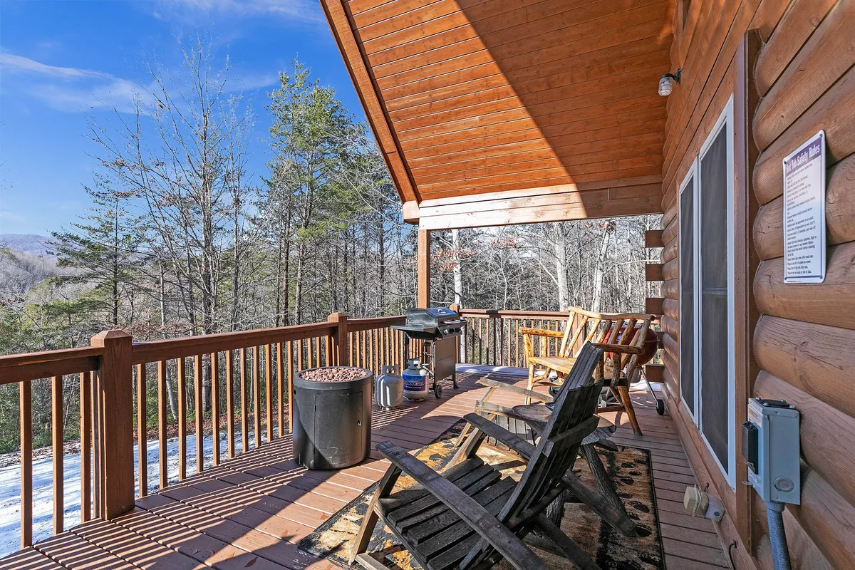 A wooden deck equipped with Adirondack chairs, a grill, and surrounded by leafy trees, this image conveys the inviting outdoor living spaces perfect for relaxation, socializing, and admiring the changing mountain scenery.