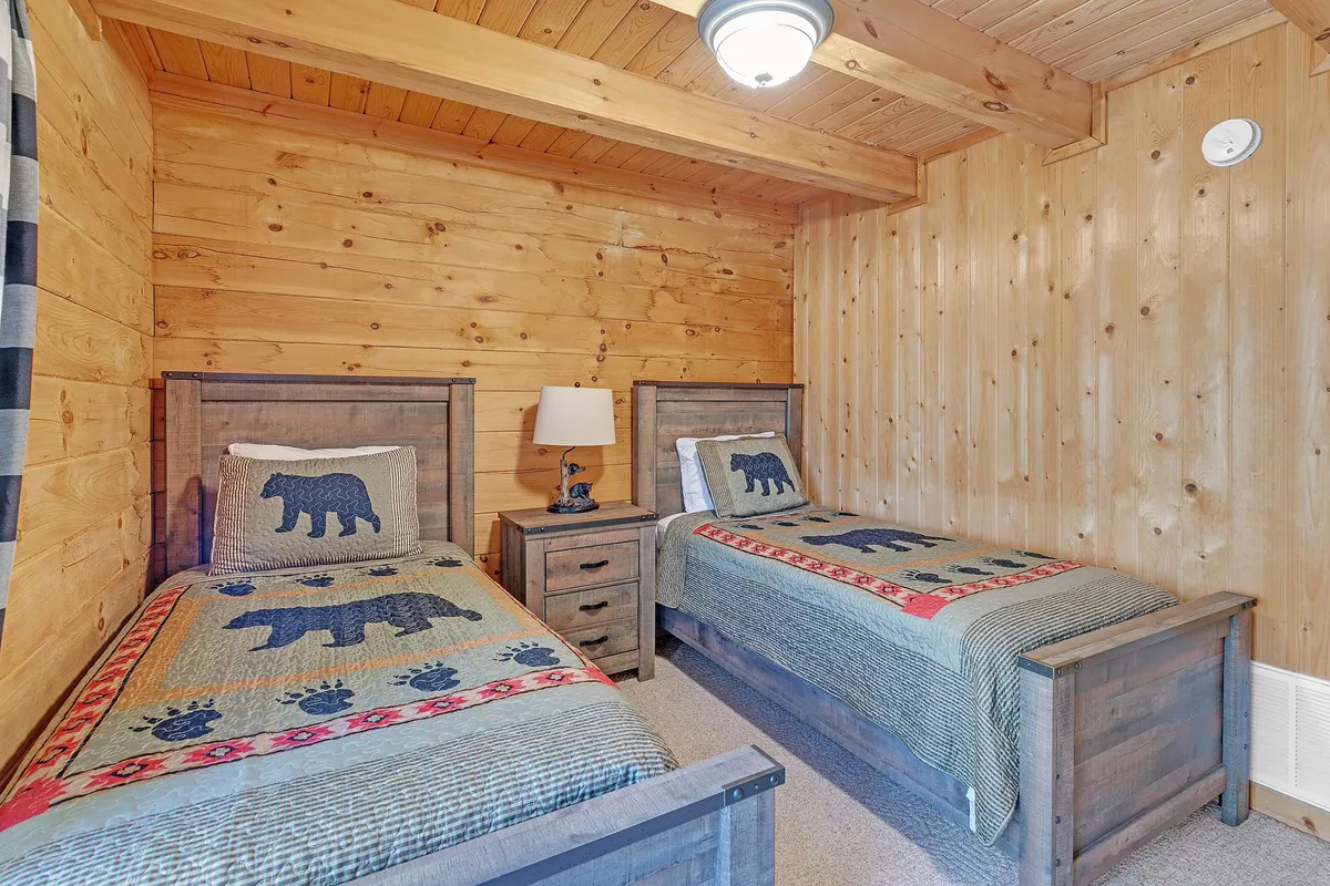 This room contains two twin beds with a nightstand and lamp in between, all surrounded by warm wooden walls. The scene feels peaceful and is perfectly suited for restful nights or quiet reading before bed.