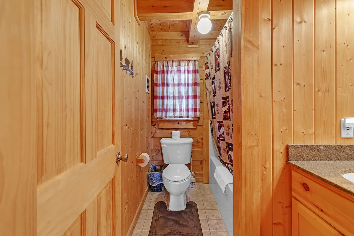 A bright bathroom with a toilet, sink, shower curtain, window, and distinctive wood paneling. The atmosphere is clean and inviting, reflecting the practicality and comfort of the basement amenities.
