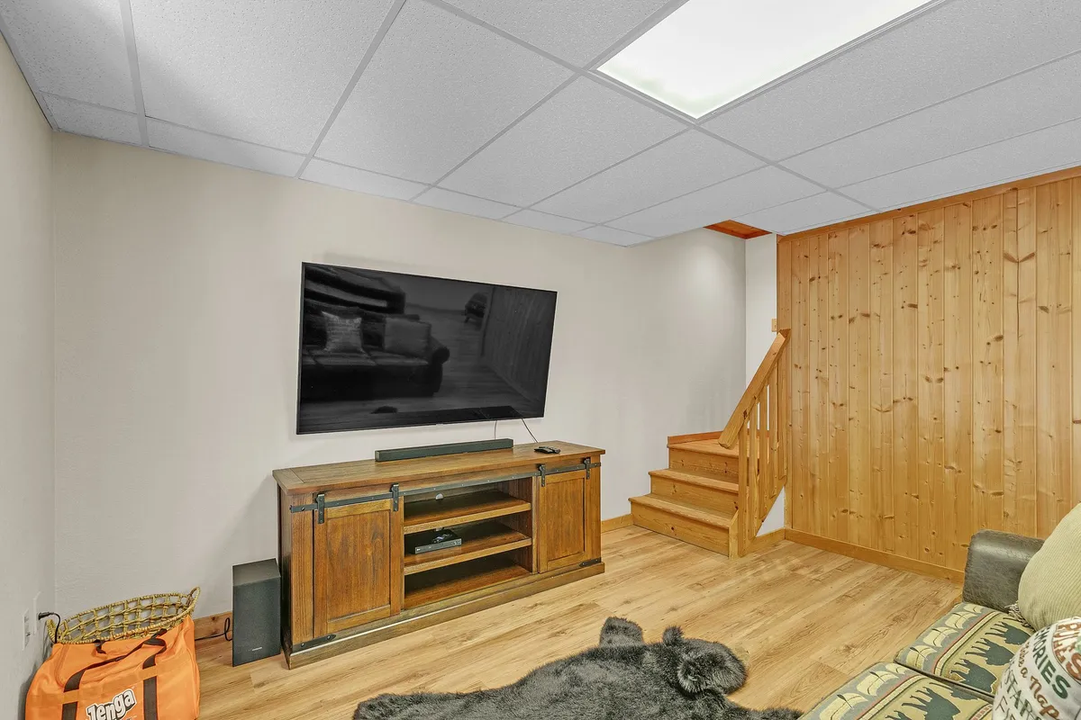 A cozy living room featuring a television as the centerpiece, framed by a wooden staircase and a rustic cabinet. Plush seating invites relaxation, and soft, natural light enhances the warm, inviting mood. The open layout suggests easy flow to adjacent spaces, ideal for gatherings and entertainment.