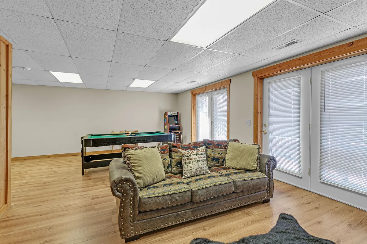 This image captures a vibrant basement family room with a sofa adorned with decorative pillows, a prominent pool table, and large windows that fill the space with natural light. The scene radiates casual comfort, inviting social interaction and relaxation.